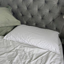 White pillow on a bed with a tufted gray headboard